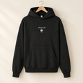 A black pullover hoodie hanging on a wooden hanger against a warm beige background. The hoodie features a small white graphic on the center chest with the text 'A New Leaf' and a leaf illustration.